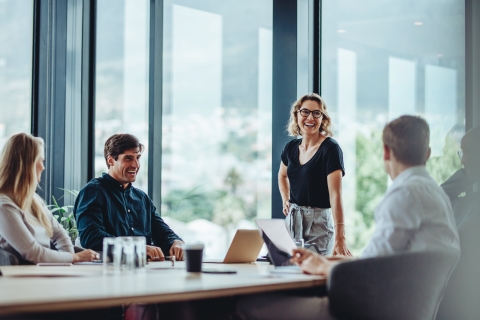 Woman standing and smiling at colleagues seated around a conference table