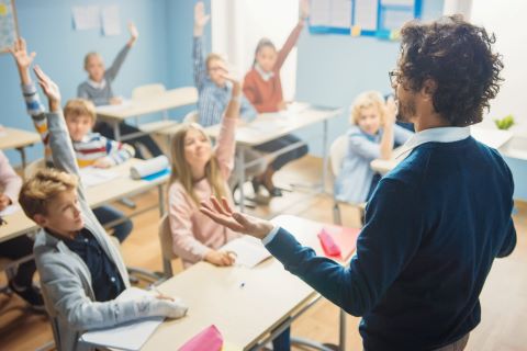 Teacher leading a classroom with students raising their hands